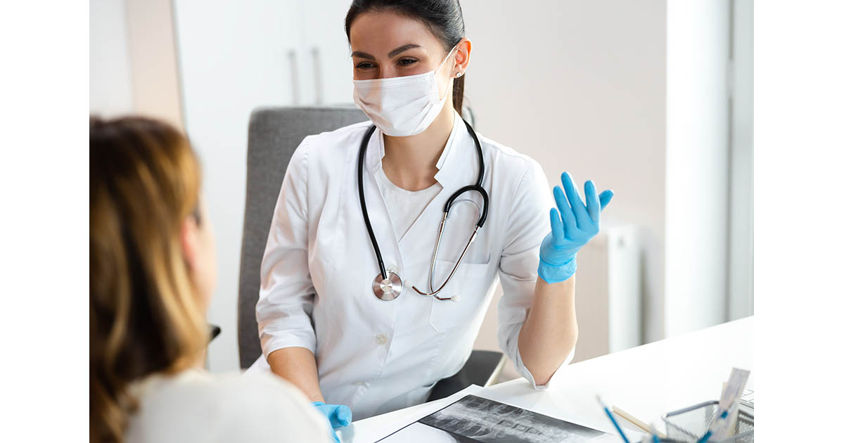 Pediatrician in a clinical office discussing a spine X-ray with a parent, with an adolescent patient seated nearby during a scoliosis evaluation