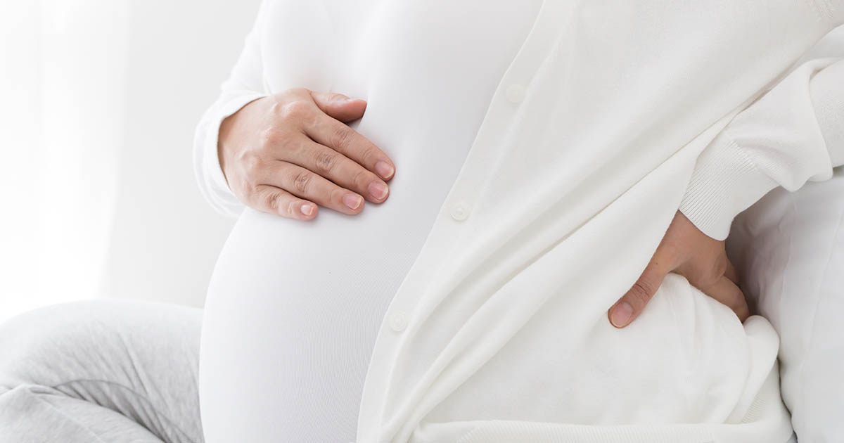Pregnant woman pressing both hands into her lower back in pain, illustrating the lumbar discomfort that affects most pregnancies