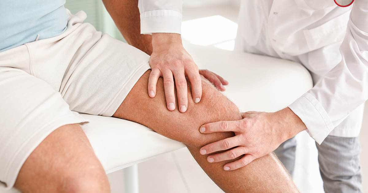 Doctor in white coat examining a patient's knee with both hands, assessing joint mobility during a clinical evaluation