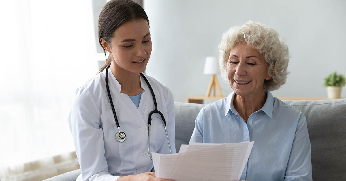 Smiling older female patient reviewing paperwork with a young female doctor in a white coat, illustrating the consultation process when discussing care options and insurance at a chiropractic clinic