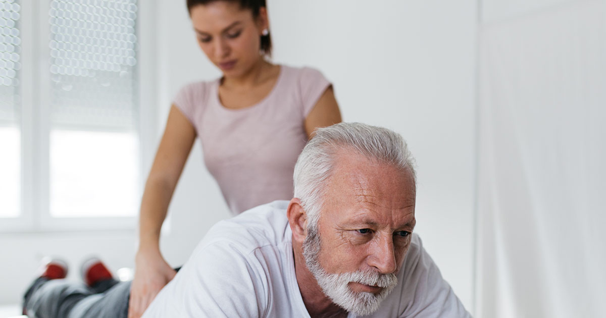 Senior man receiving gentle chiropractic back treatment from a practitioner in a bright clinical setting