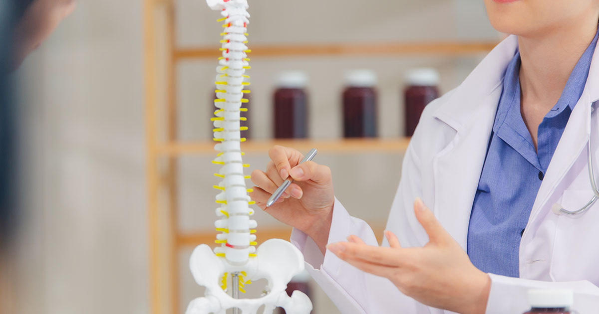 Doctor in white coat pointing at an anatomical spinal model during a patient consultation about back pain treatment options