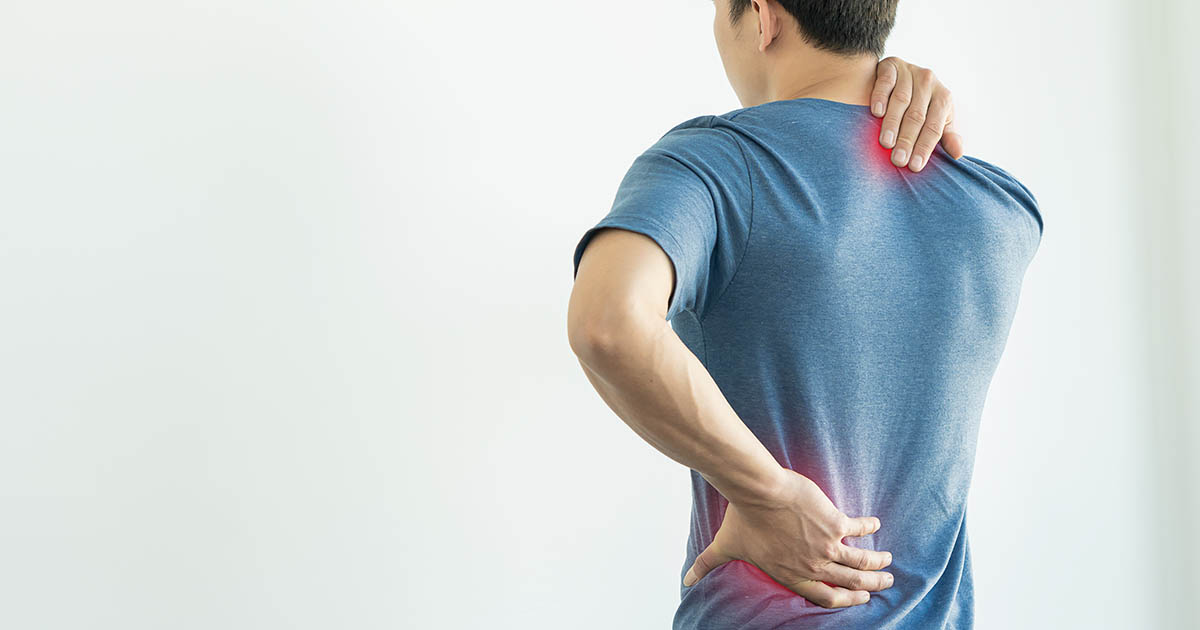 Man standing with back turned, hands on shoulder and lower back, with red glow at pain points illustrating chronic inflammation