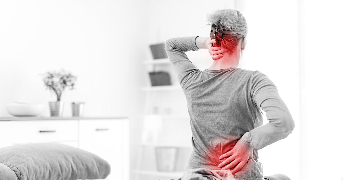 Person sitting on the edge of the bed, gripping their lower back and neck with red pain indicator overlays, illustrating how chronic back pain disrupts sleep and causes morning stiffness