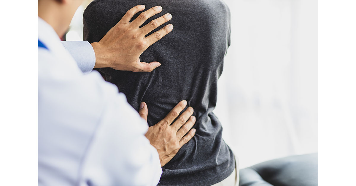 Doctor examining a seated patient's lower back in a clinical examination room