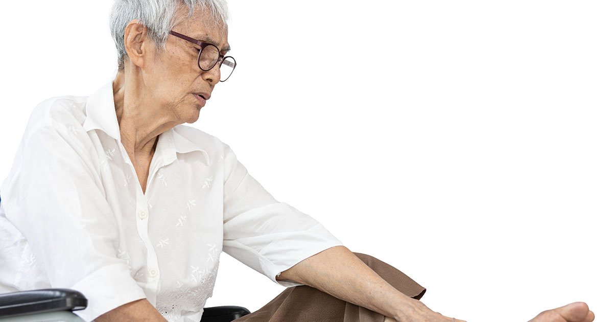 Elderly woman seated and examining her foot and ankle, showing signs of lower limb nerve weakness