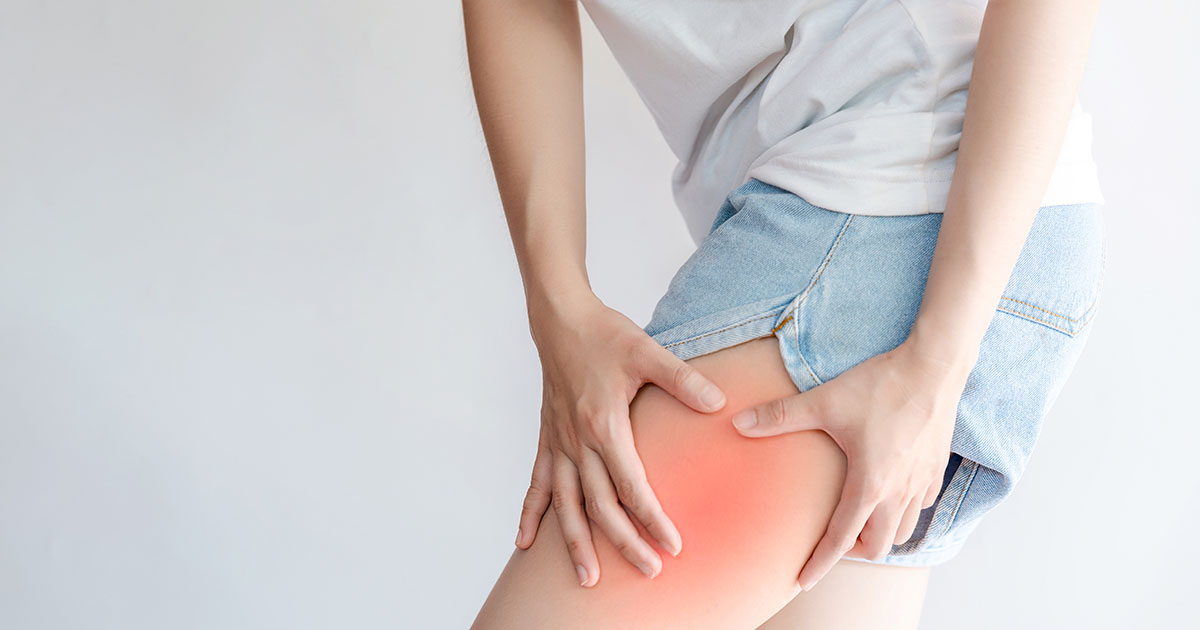 Woman sitting and reaching down to her upper thigh, feeling anterior thigh pain that may originate from lumbar disc compression