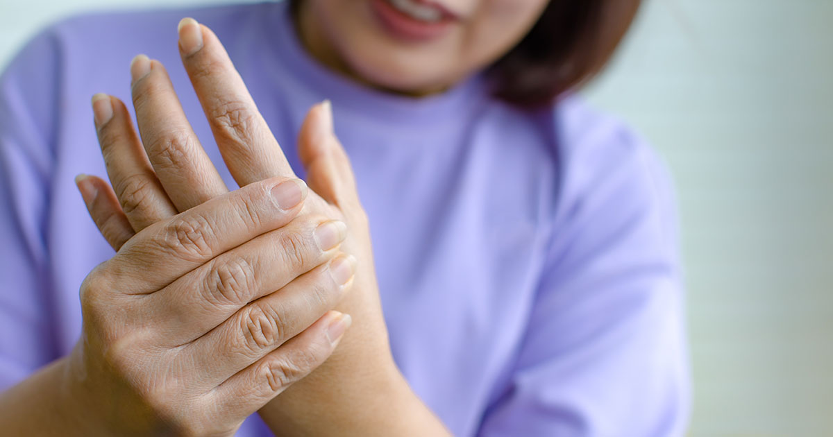 Woman looking at her palm with a pained expression, holding her hand as she examines tingling and numbness at night