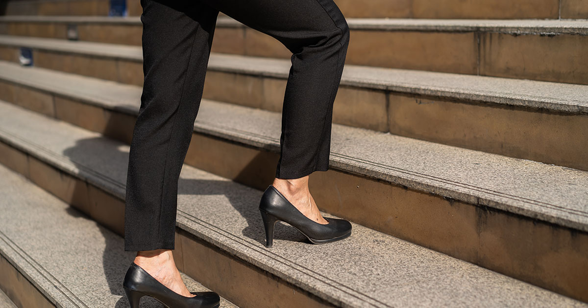 Business woman in black high heels climbing stone stairs, illustrating how heel elevation shifts posture and loads the lower back