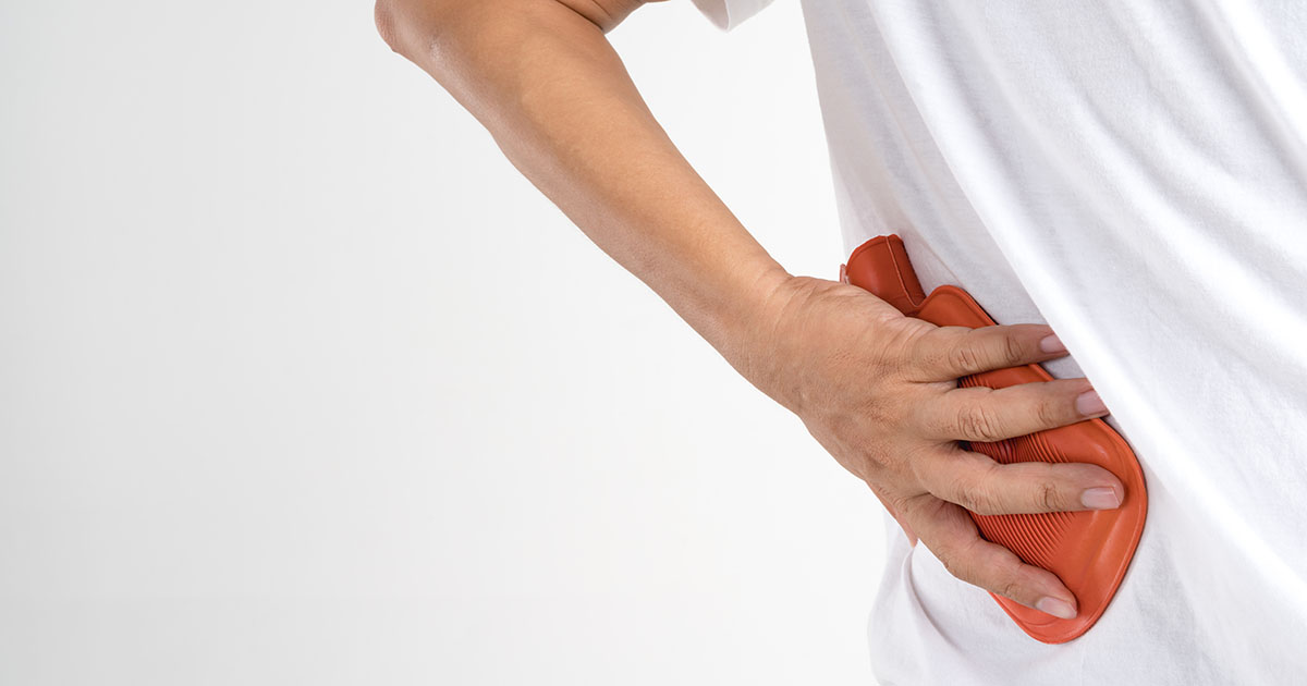 Person pressing a red hot water bottle against their lower back for pain relief