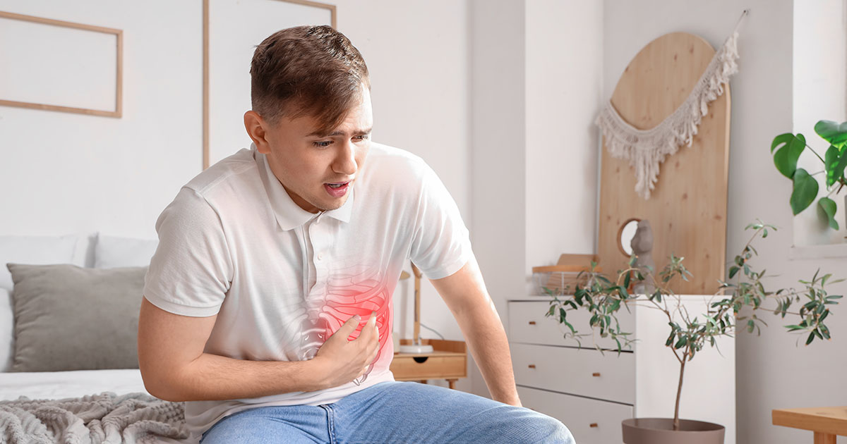 Man sitting on bed gripping his left side rib area in pain with a red pain indicator highlighting the intercostal region
