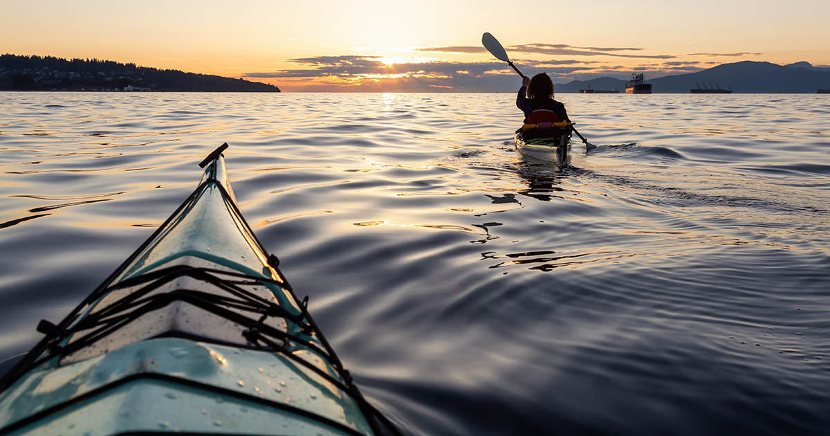 Two women stand-up paddleboarding on crystal clear blue water under a bright summer sky