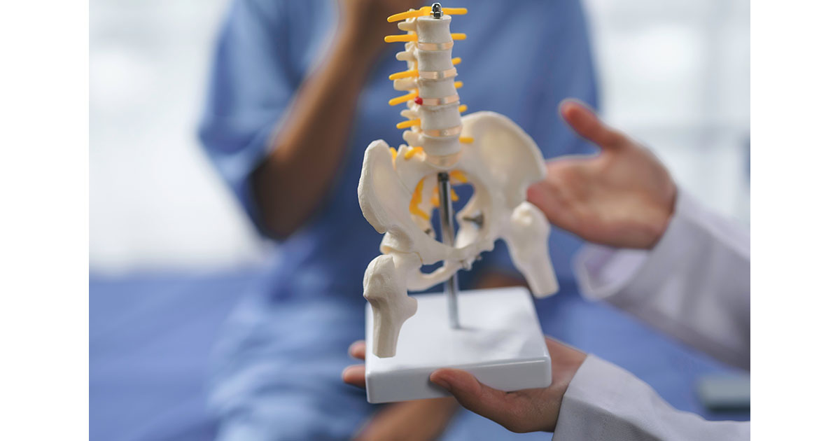 Doctor pointing to anatomical pelvis and spine model while explaining leg length discrepancy and pelvic alignment to a patient in a clinical consultation