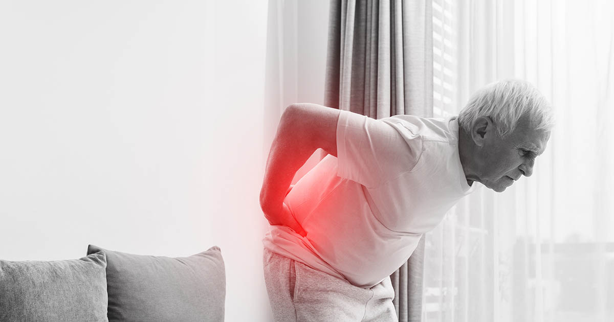 African American woman in a striped shirt leaning back from her laptop with a pained expression, pressing her hand firmly into her lower back, illustrating the posture-driven lower back pain of lower cross syndrome