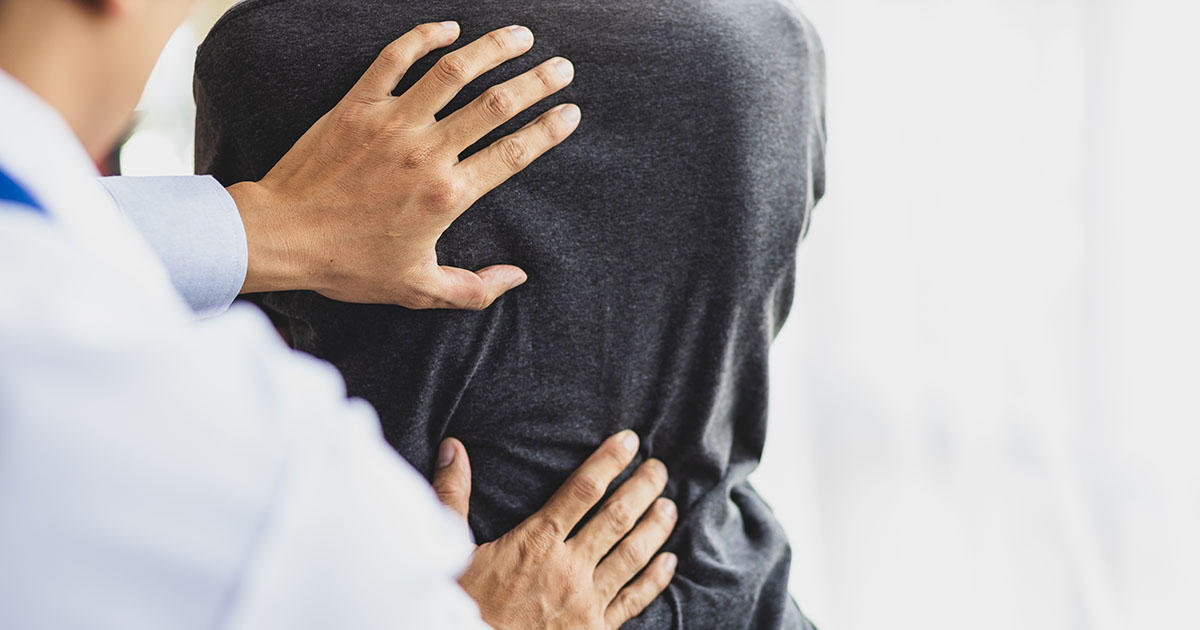 A chiropractor's hands examining a patient's lower back during a movement assessment to evaluate flexion and extension pain patterns