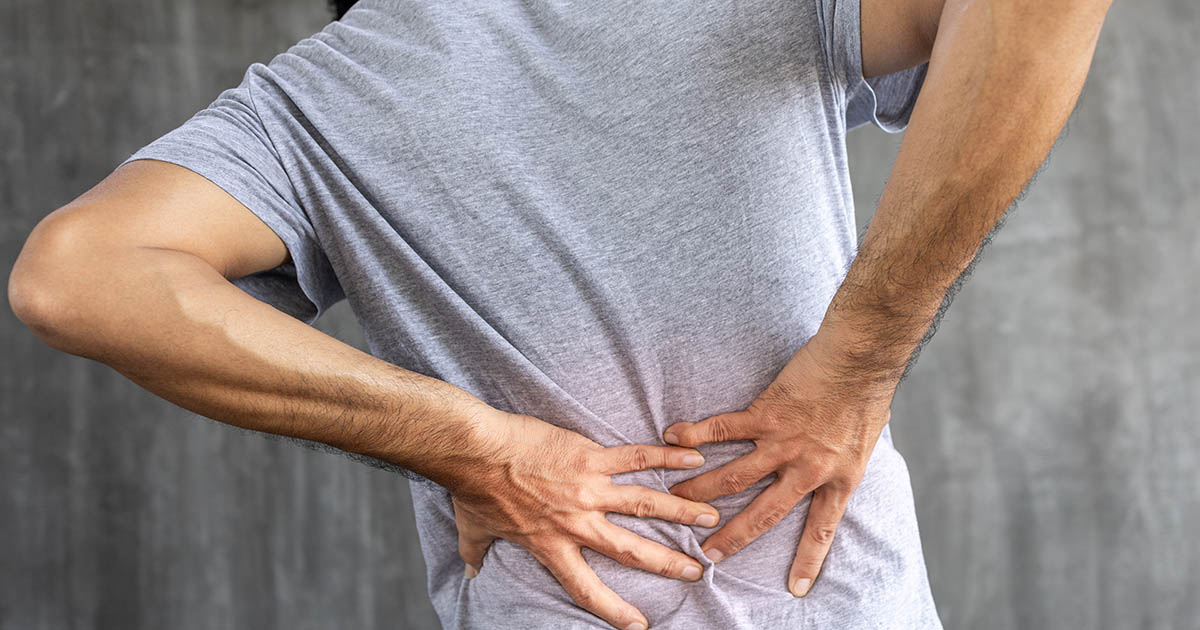 Man holding his lower back with both hands, showing the acute pain of a lower back episode giving out