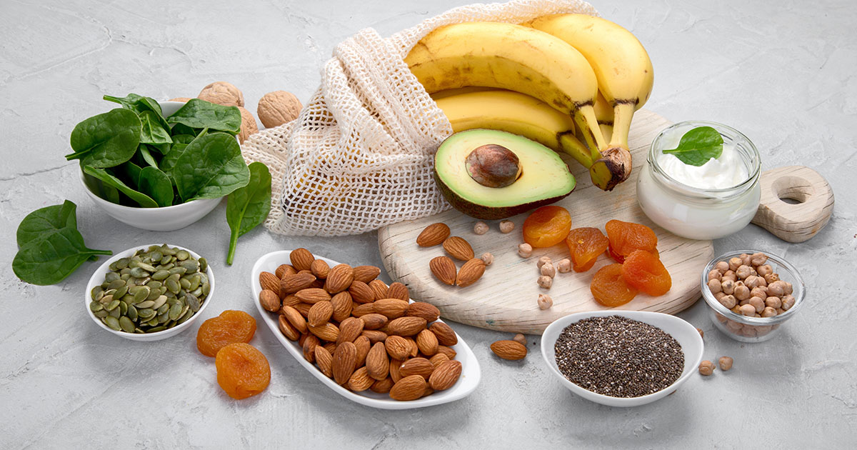 Colorful assortment of magnesium-rich foods and mineral supplements laid out on a light surface, including dark leafy greens, nuts, seeds, and magnesium capsules