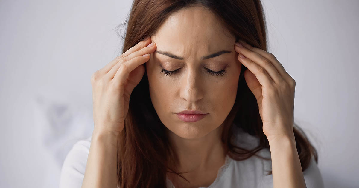 Woman with closed eyes pressing her fingers to her temples while experiencing a migraine headache