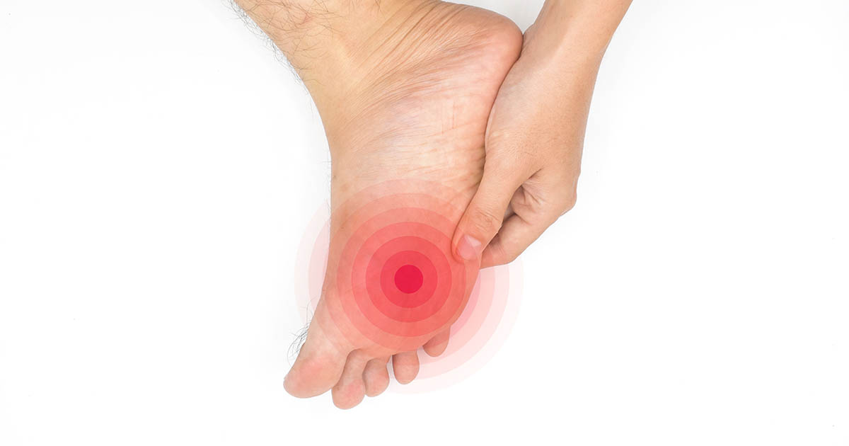 Man gripping the ball of his foot with a red radiating pain indicator between the third and fourth toes, illustrating the location of Morton's neuroma nerve compression