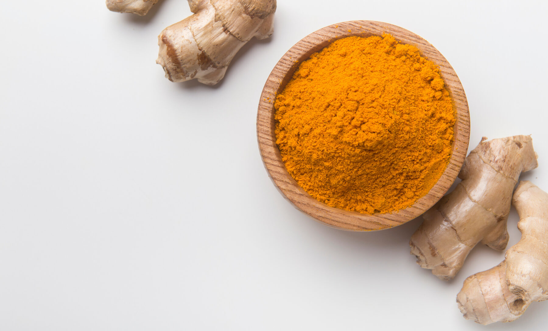 Turmeric powder in a wooden bowl alongside fresh turmeric root, a natural anti-inflammatory ingredient studied for back pain and spinal inflammation