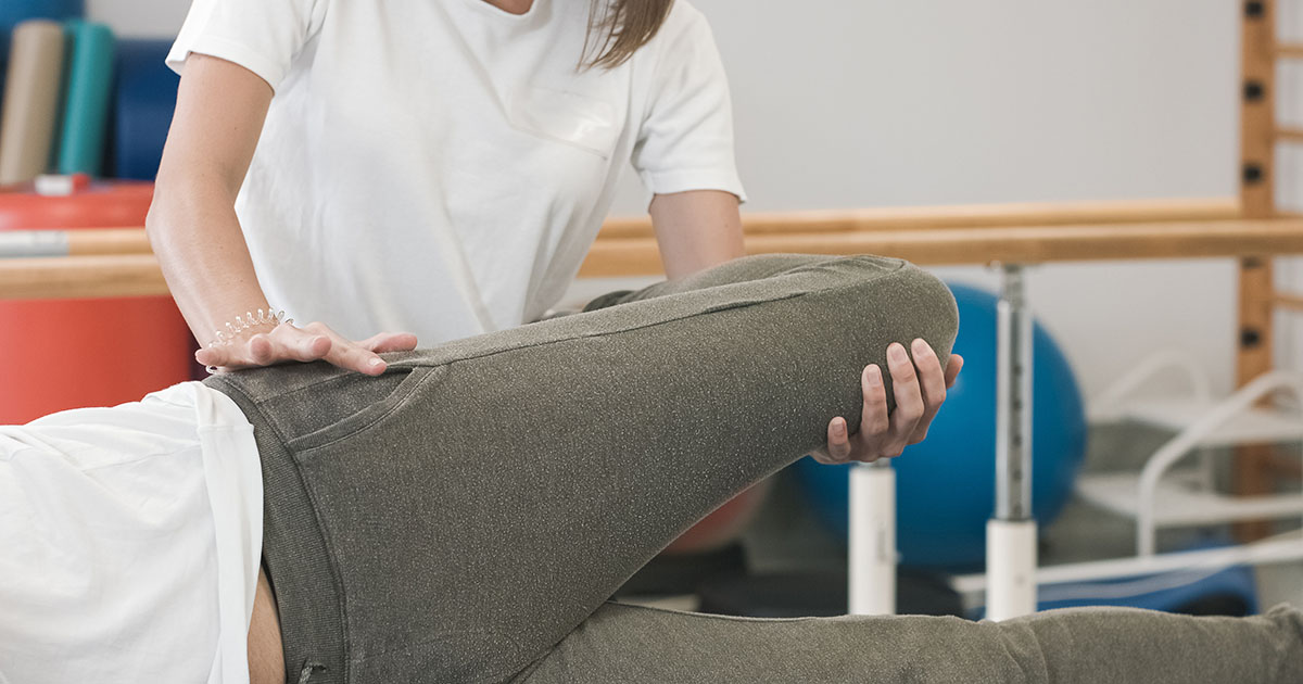 Physical therapist guiding a patient through a leg-raise nerve mobilization exercise on a treatment table in a clinic