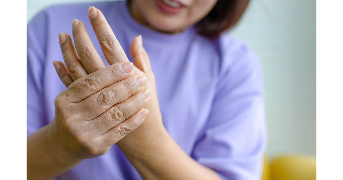 Woman seated and holding her palm with an expression of tingling pain, illustrating the hand nerve symptoms used to distinguish nerve pain from muscle soreness