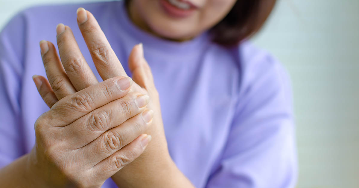 Woman in a lavender top holding her wrist and closely examining her tingling, numb palm, illustrating the hand symptoms of peripheral neuropathy