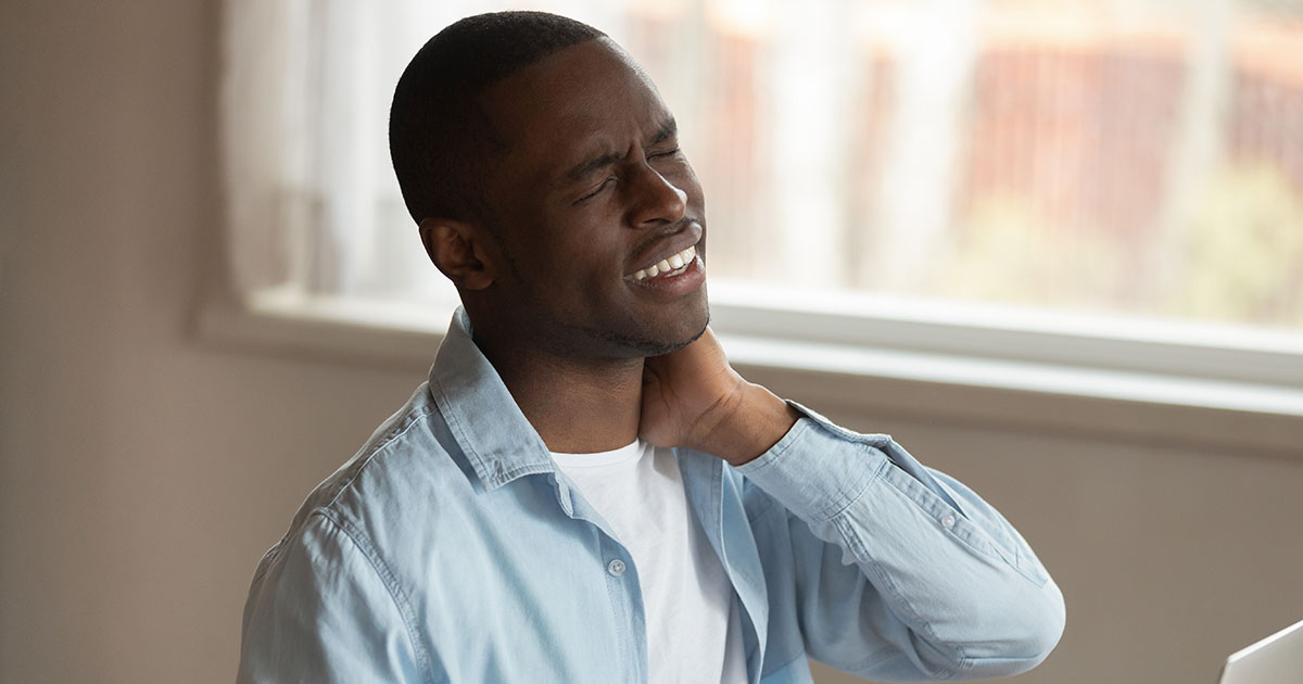 Man gripping the back of his neck in pain while seated at a desk, depicting the sharp localized discomfort of a cervical pinched nerve