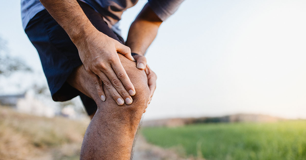 Sporty man gripping his knee in pain on a running track after sustaining an injury during a training session, illustrating the real pain of a workout injury versus normal post-exercise muscle soreness
