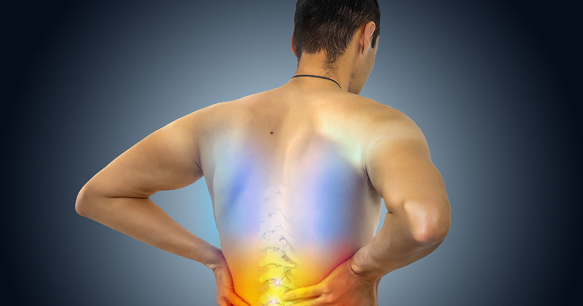 Middle-aged man in a white t-shirt wincing as he presses his hand against his lower back on one side, illustrating the one-sided pain pattern typical of quadratus lumborum strain