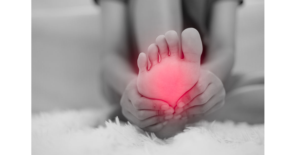 Woman sitting on the edge of a couch at home, holding her bare foot with an expression of discomfort from nerve tingling
