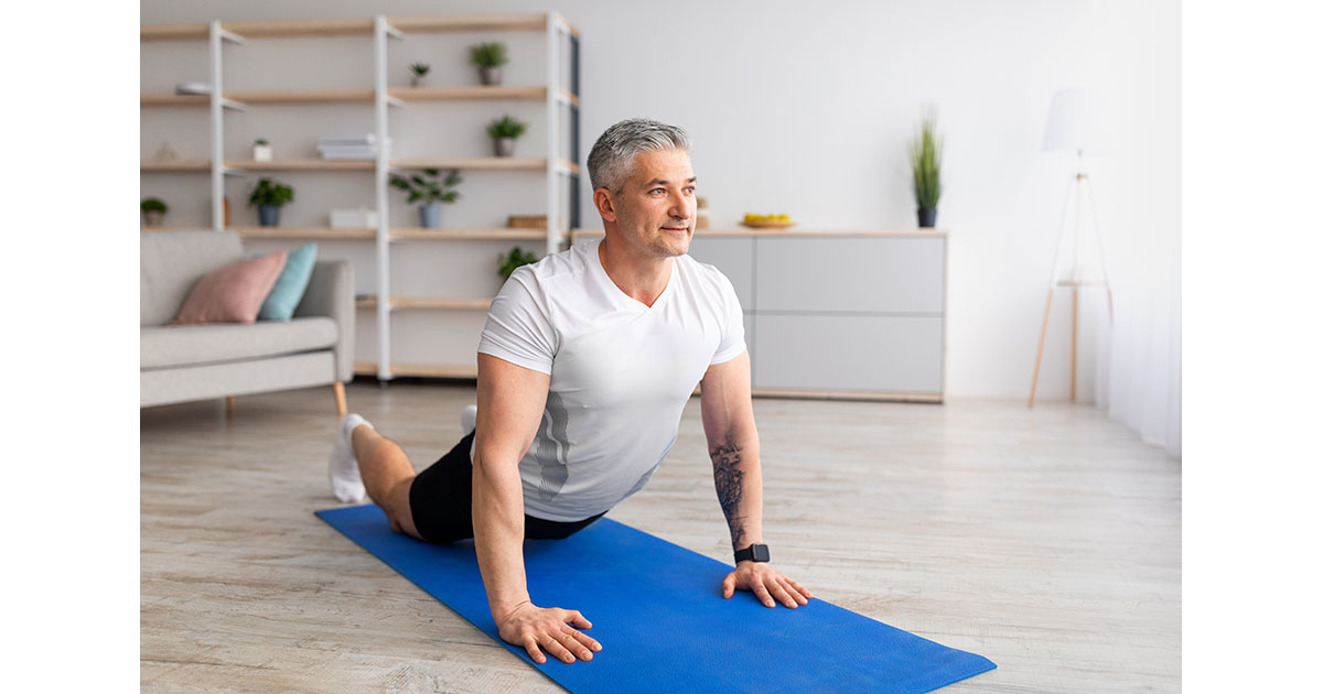 Middle-aged man performing a cobra back extension stretch on a yoga mat at home, a common first exercise after a back pain flare