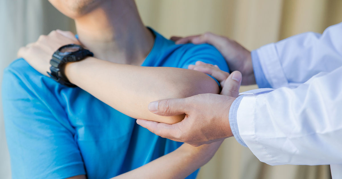 Doctor in white coat examining a patient's shoulder and upper arm during a clinical evaluation for shoulder bursitis