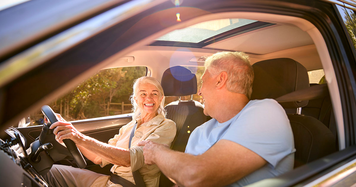 Older couple smiling together in a car during their road trip south to Florida for snowbird season
