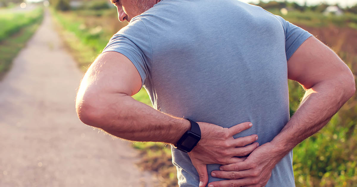 Active man gripping his lower back in pain on an outdoor walking path, illustrating the back pain that worsens with walking in lumbar spinal stenosis