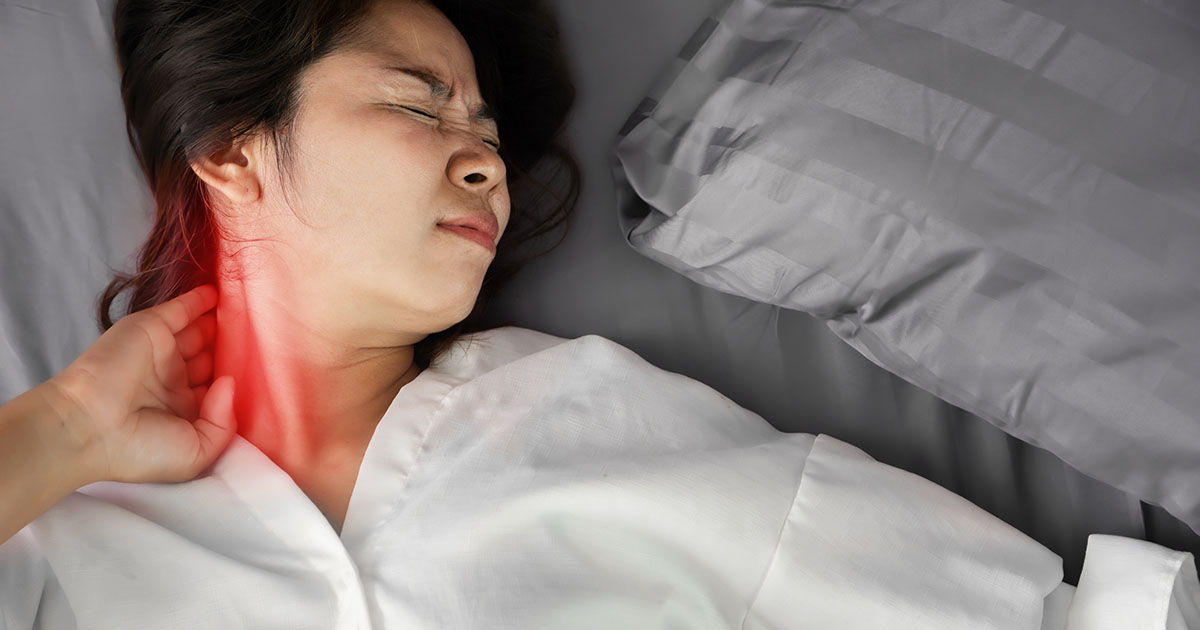 Woman lying in bed holding her neck in pain, red highlighting on neck indicating neck strain from sleeping in an awkward position