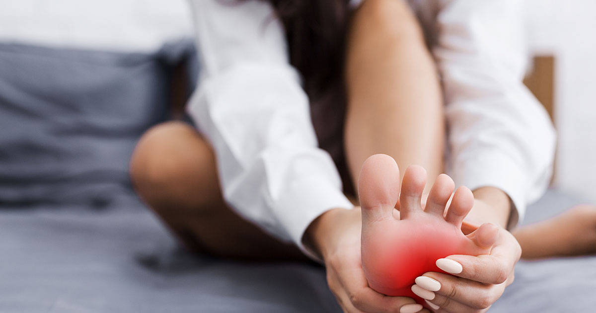 Close-up of a person gripping their inner ankle and heel in pain, illustrating the nerve compression and burning sensation of tarsal tunnel syndrome
