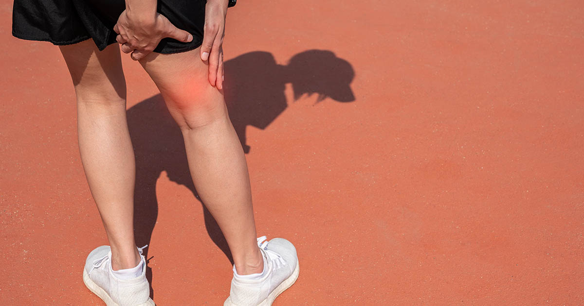 Female runner on an outdoor track holding her hamstring area, illustrating tight hamstring pain and its connection to lower back problems