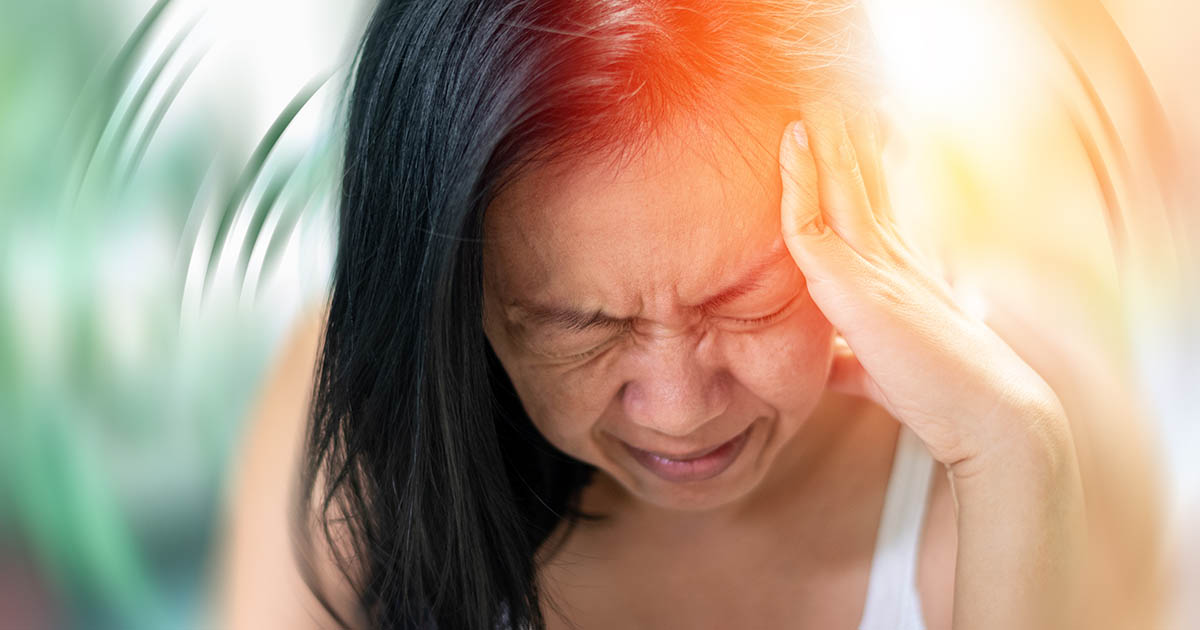Woman wincing with eyes closed and a hand pressed to her temple, motion-blur lines radiating around her conveying the spinning sensation of vertigo