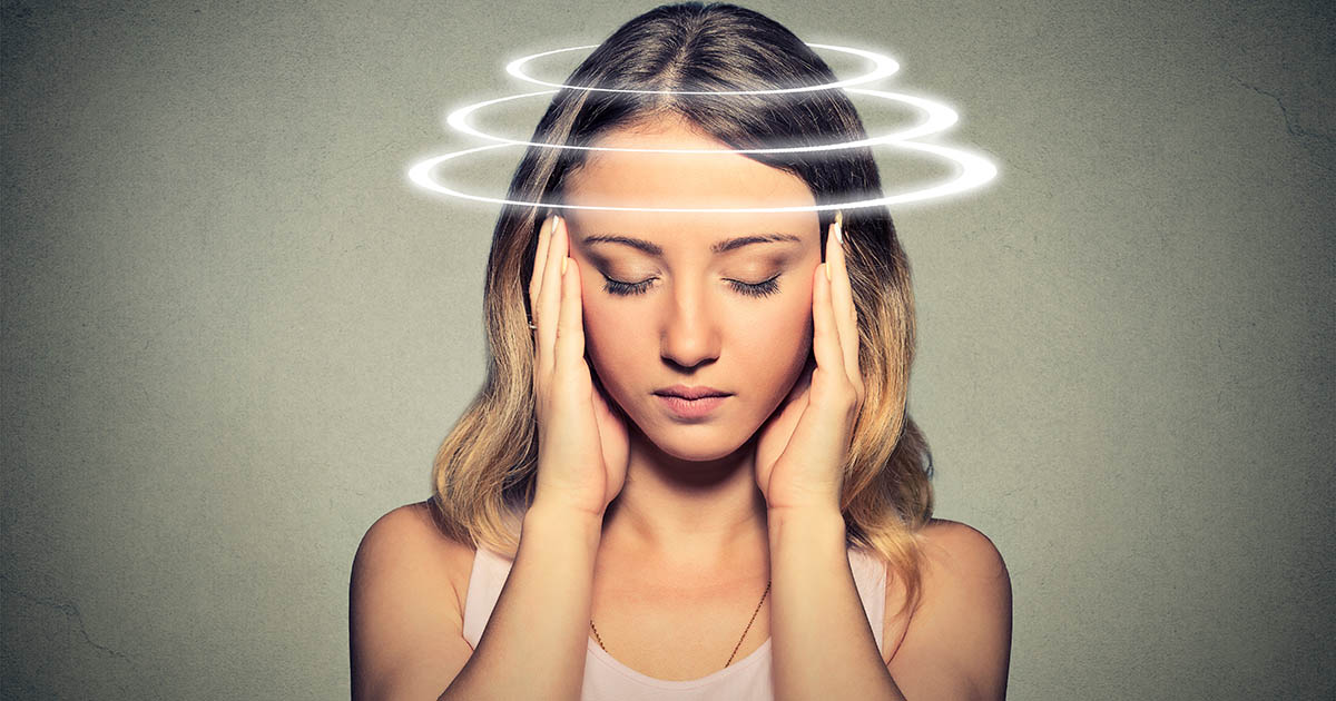 Woman wincing with eyes closed and a hand pressed to her temple, motion-blur lines radiating around her conveying the spinning sensation of vertigo