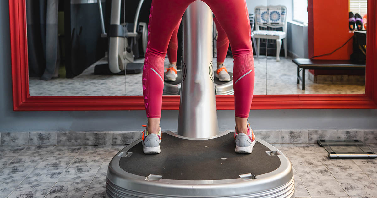 Person standing on a whole body vibration platform in a clinical wellness setting, used for neuromuscular stimulation and spine rehabilitation