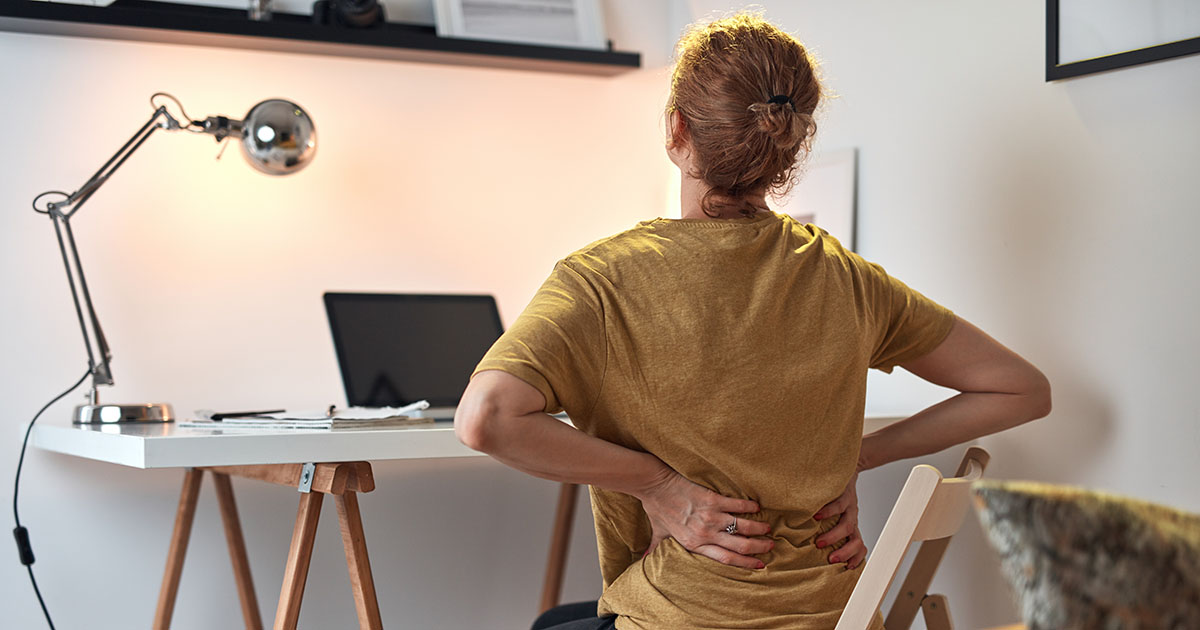 Young woman at a home office desk with a laptop, eyes closed, holding her neck in pain from poor posture and prolonged sitting