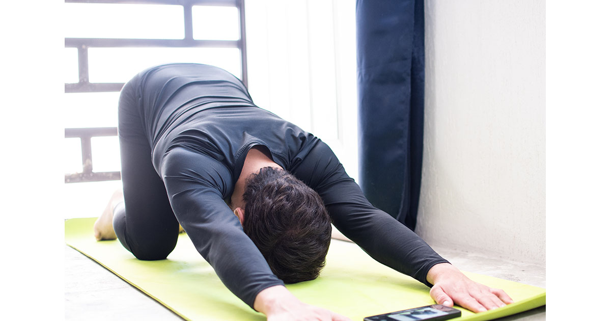Woman in athletic wear doing a cobra-pose spinal extension stretch on a purple yoga mat in a home gym, illustrating a yoga pose that can relieve back pain