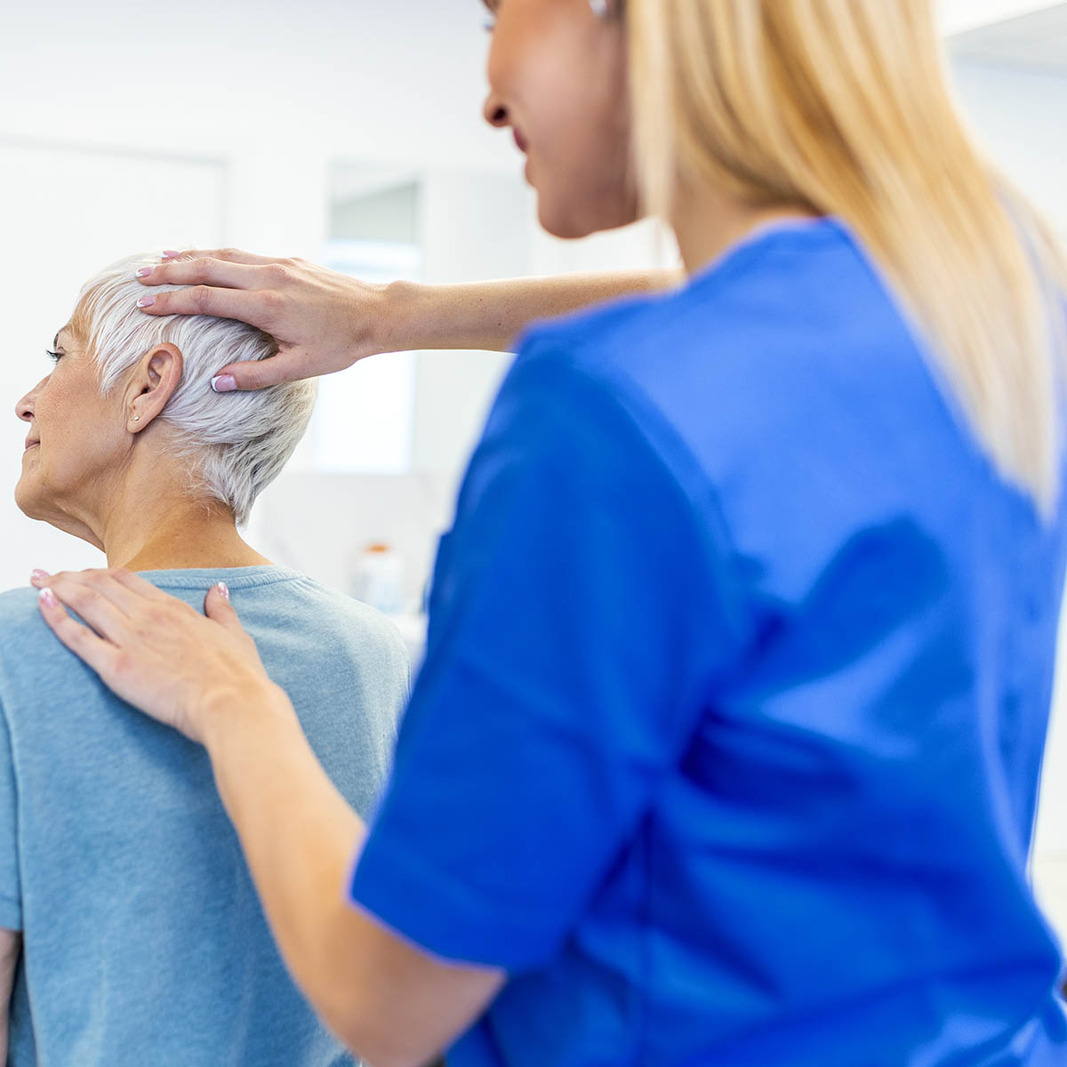 Licensed therapist gently mobilizes the upper neck and shoulder of an older female patient in a clinical office, the kind of hands-on adjustment Dr. Banman delivers at Spine & Wellness Center Lakewood Ranch