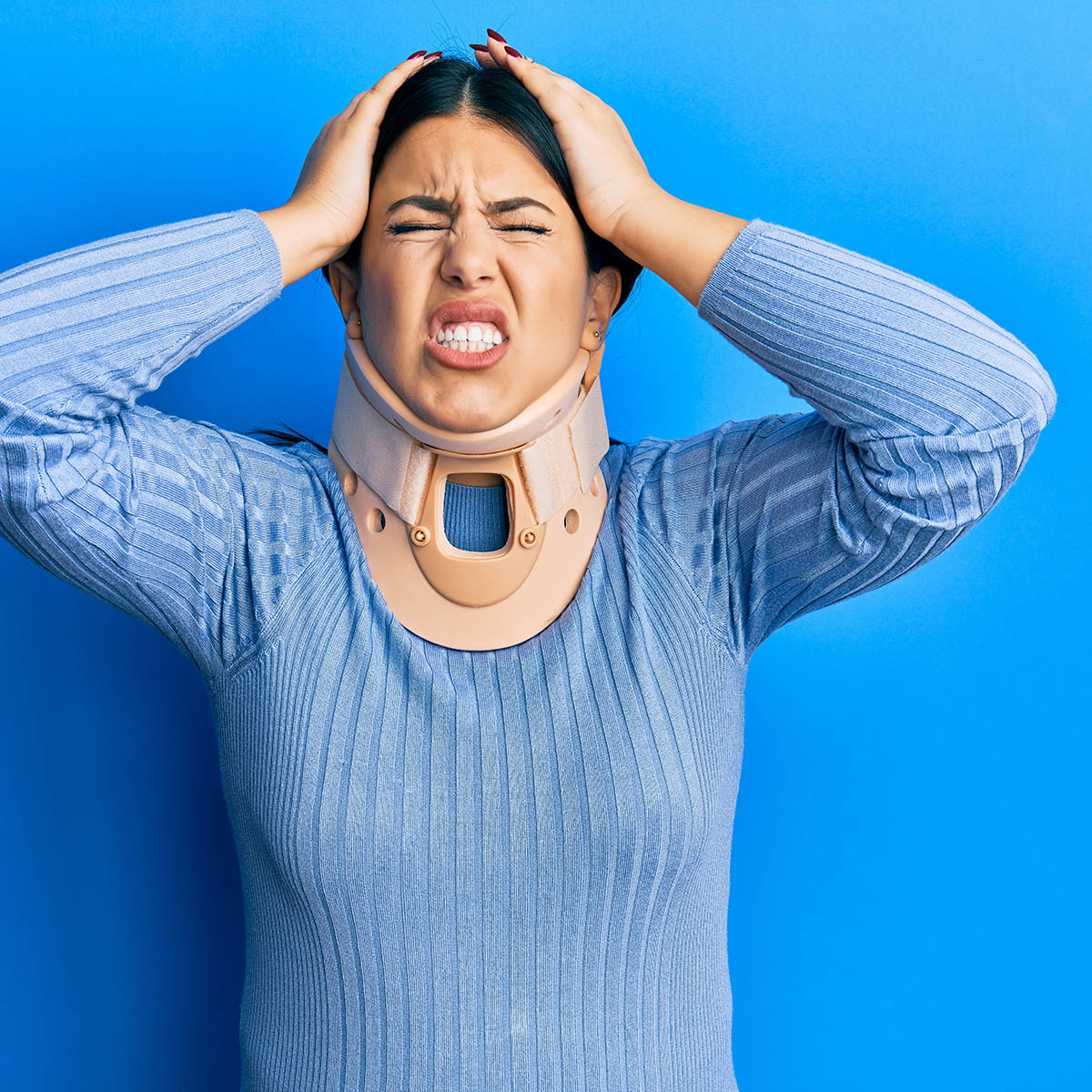 Woman pressing her temple and wearing a cervical collar, representing the cervicogenic headache pattern Dr. Banman evaluates and treats at Spine and Wellness Center Lakewood Ranch